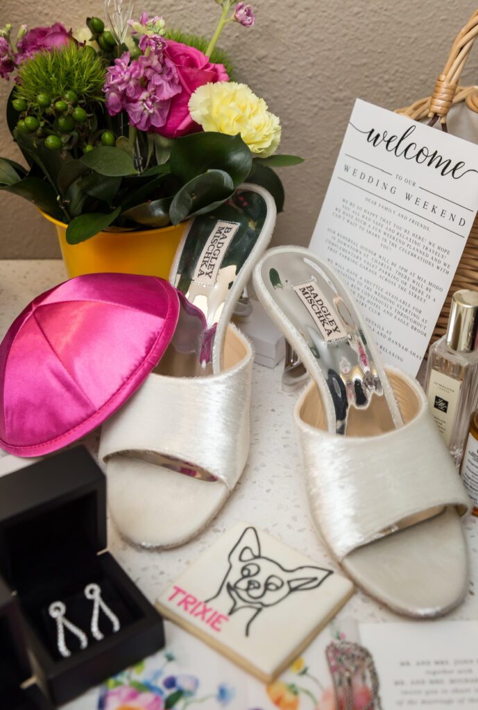 Solving Common Bridal Hair Extensions Problems Before the Big Day 1 Bridal flat lay with Badgley Mischka wedding shoes, vibrant bridal bouquet, welcome itinerary, bridal earrings, Jo Malone perfume, and satin yarmulke – perfect wedding day prep captured by OnTrend Hair & Makeup.